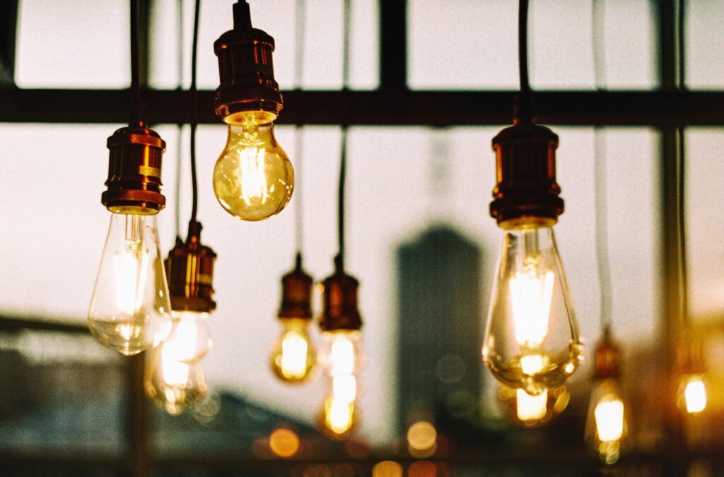 Warm-toned photo showcasing several illuminated Edison bulbs hanging indoors with a blurred cityscape in the background.